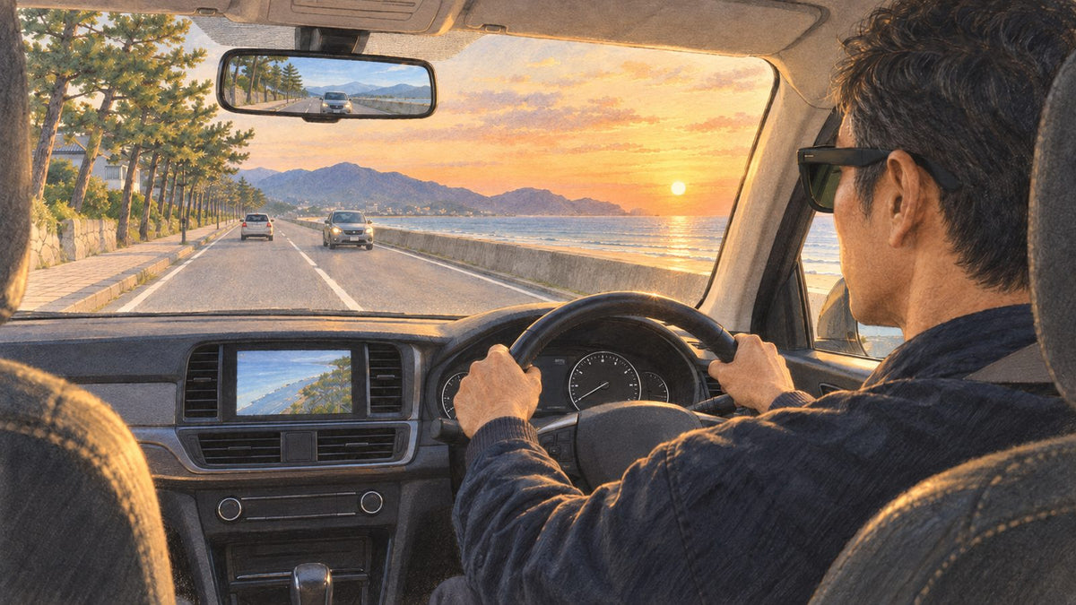 夕暮れの海沿いの道を、サングラスをかけて運転する男性の車内からの後ろ姿